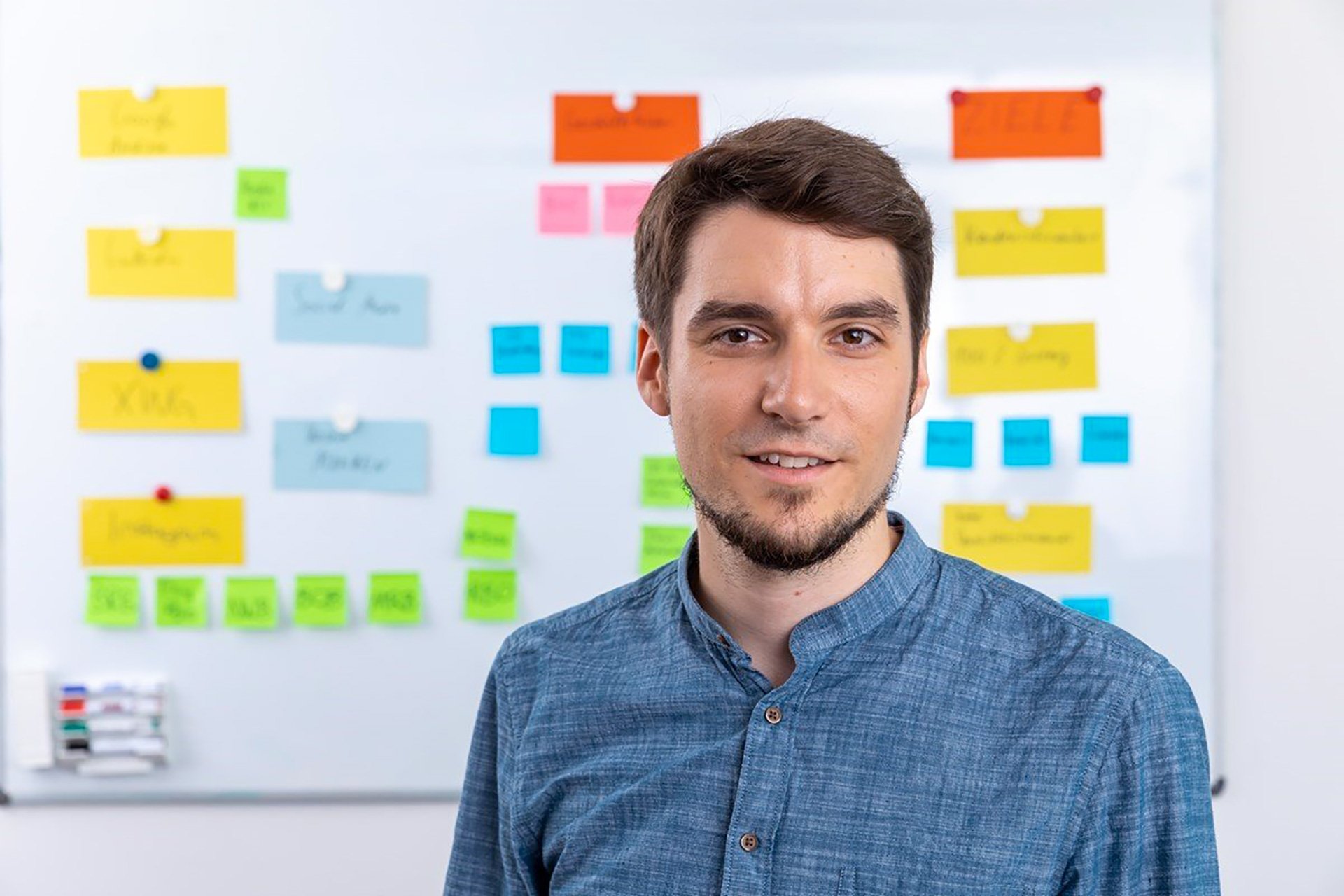 man wearing a blue shirt in front of a blurred board brainstorming marketing study