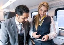 a ticket inspector checking the ticket of a male passenger dressed in a grey suit