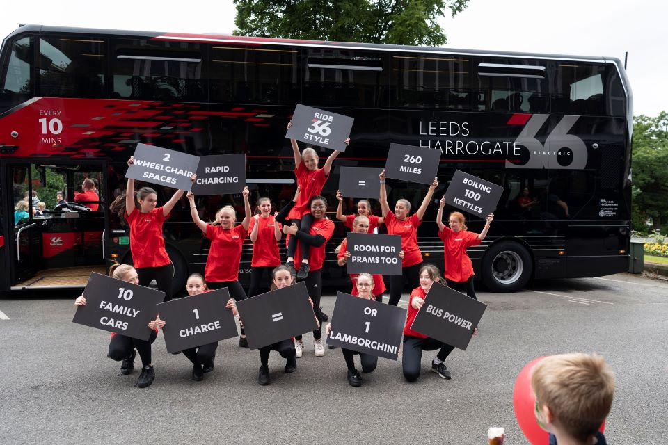 Chrildren dancing in front of Leeds Harrogate New Electric 3Buses