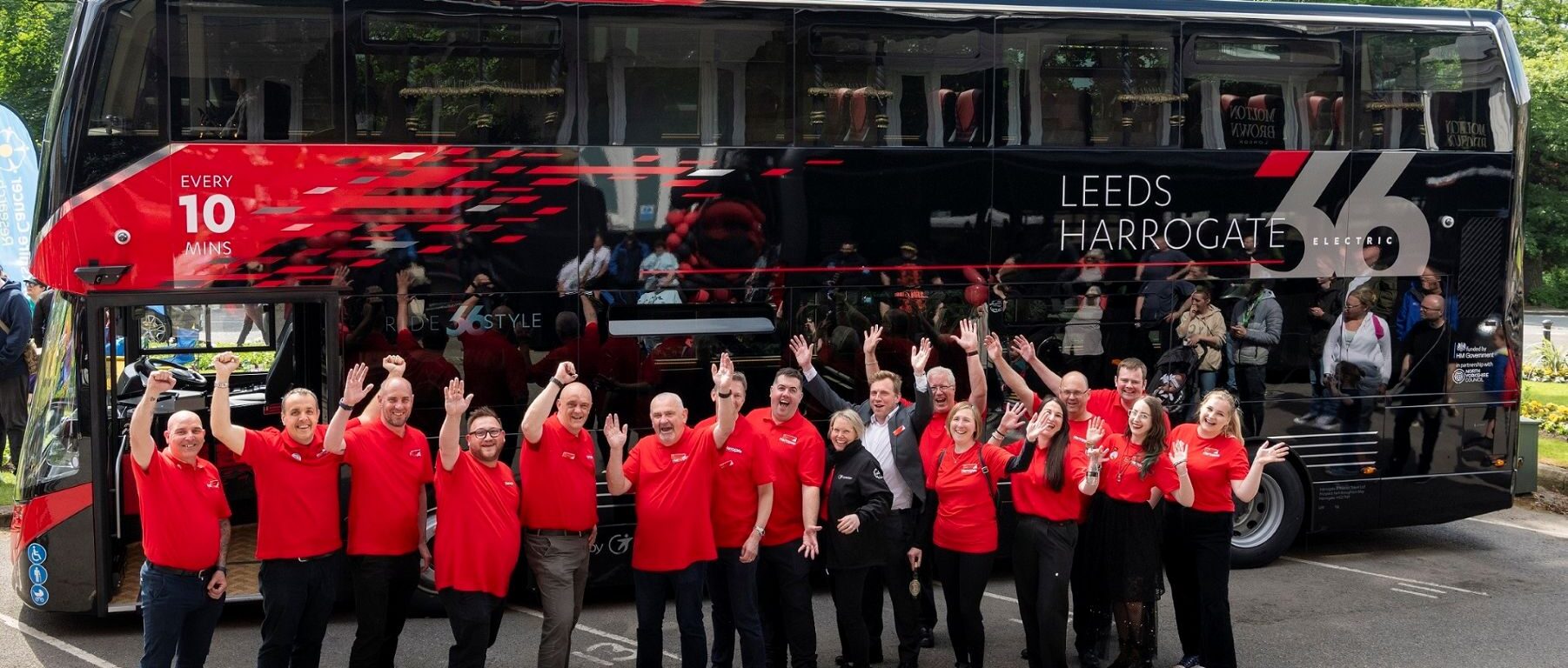 Team members of Route 26 standing in front of a bus smiling and waving